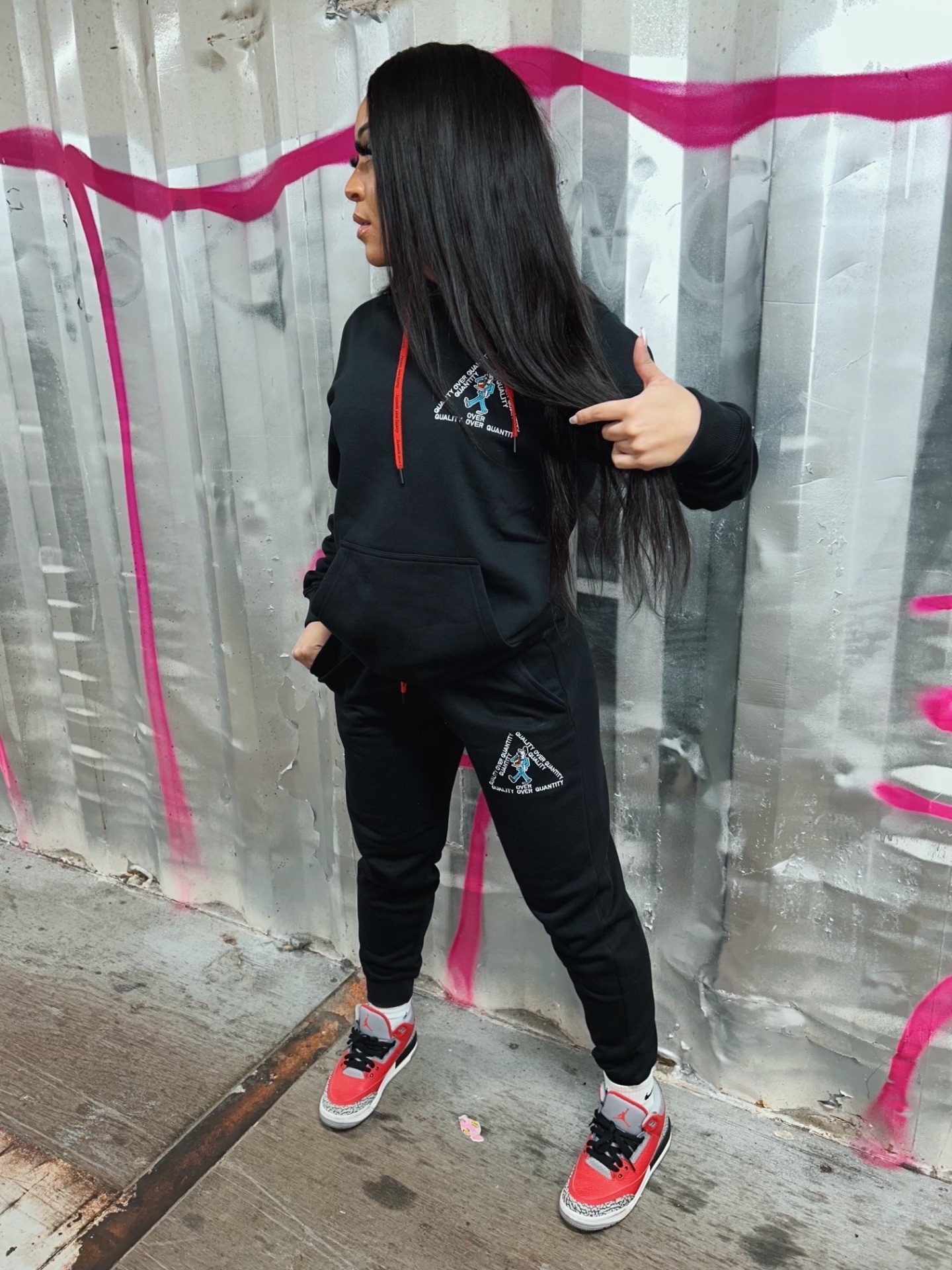 Model in PETRO QOQ black tracksuit and Air Jordans against graffiti wall