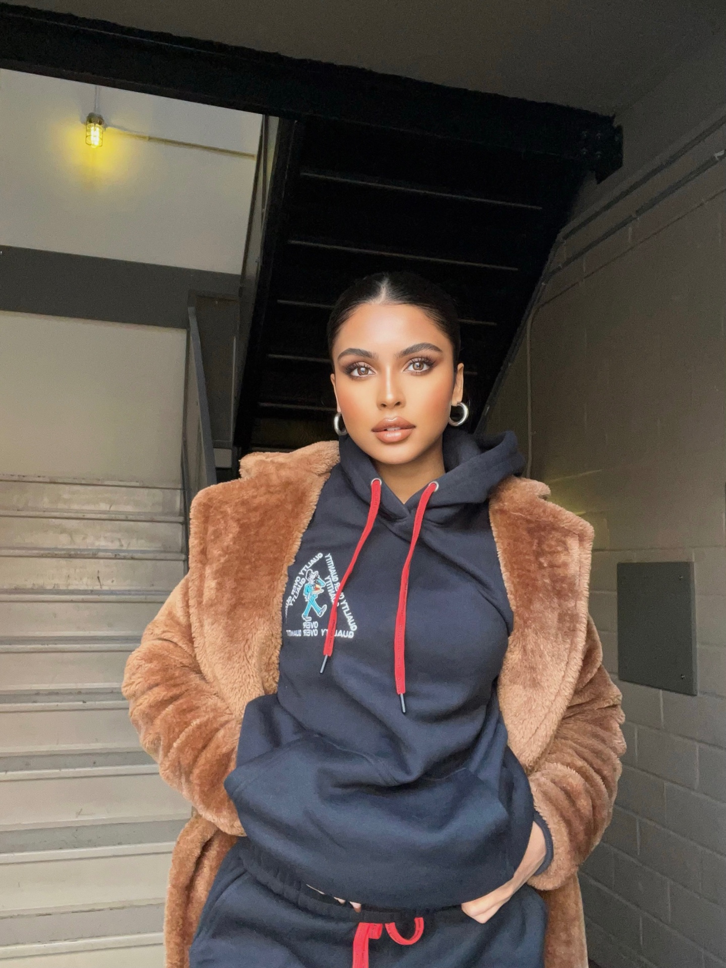Model in PETRO QOQ hoodie layered with teddy coat in industrial stairwell