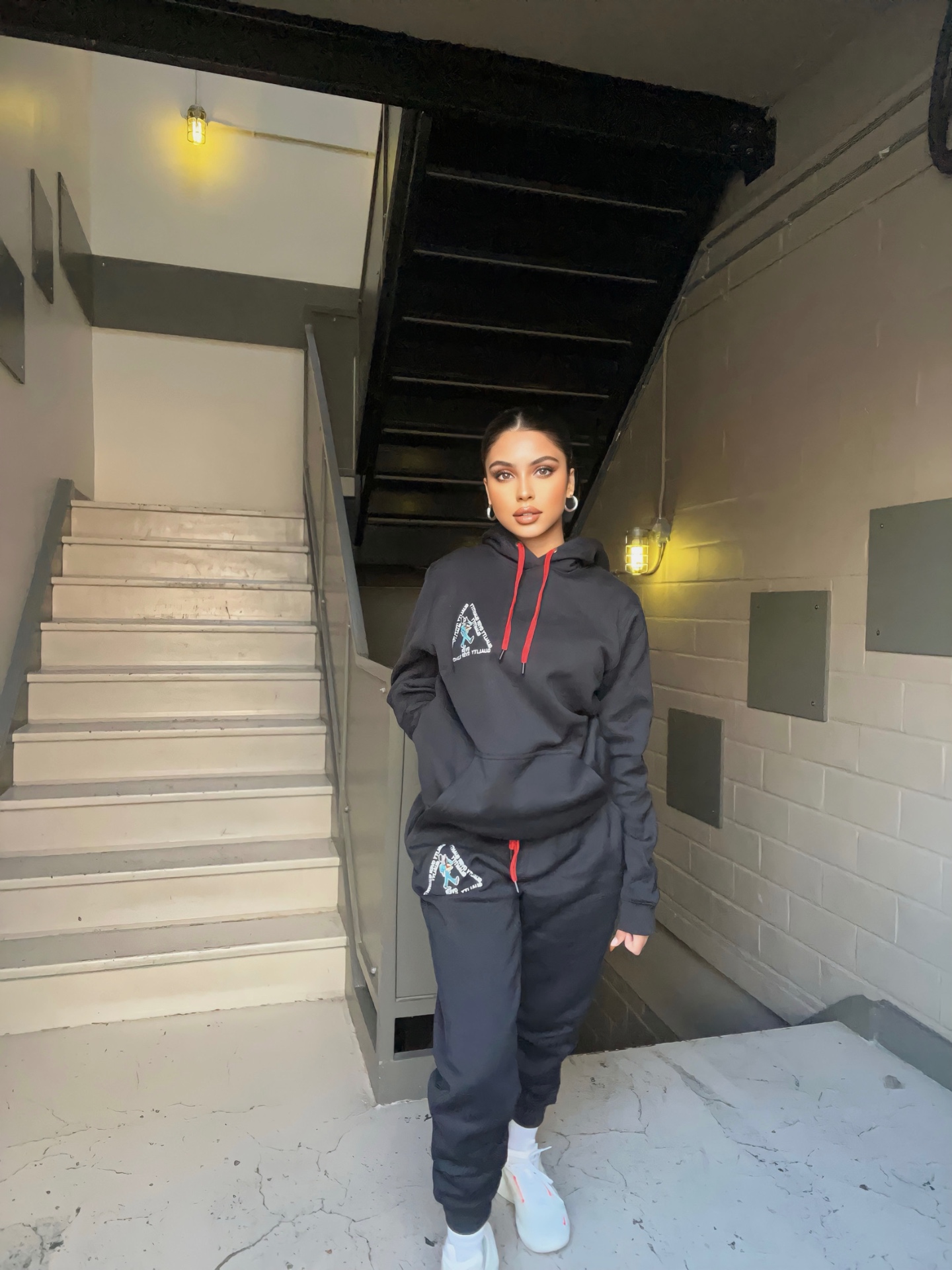 Model in PETRO QOQ black hoodie set in industrial stairwell